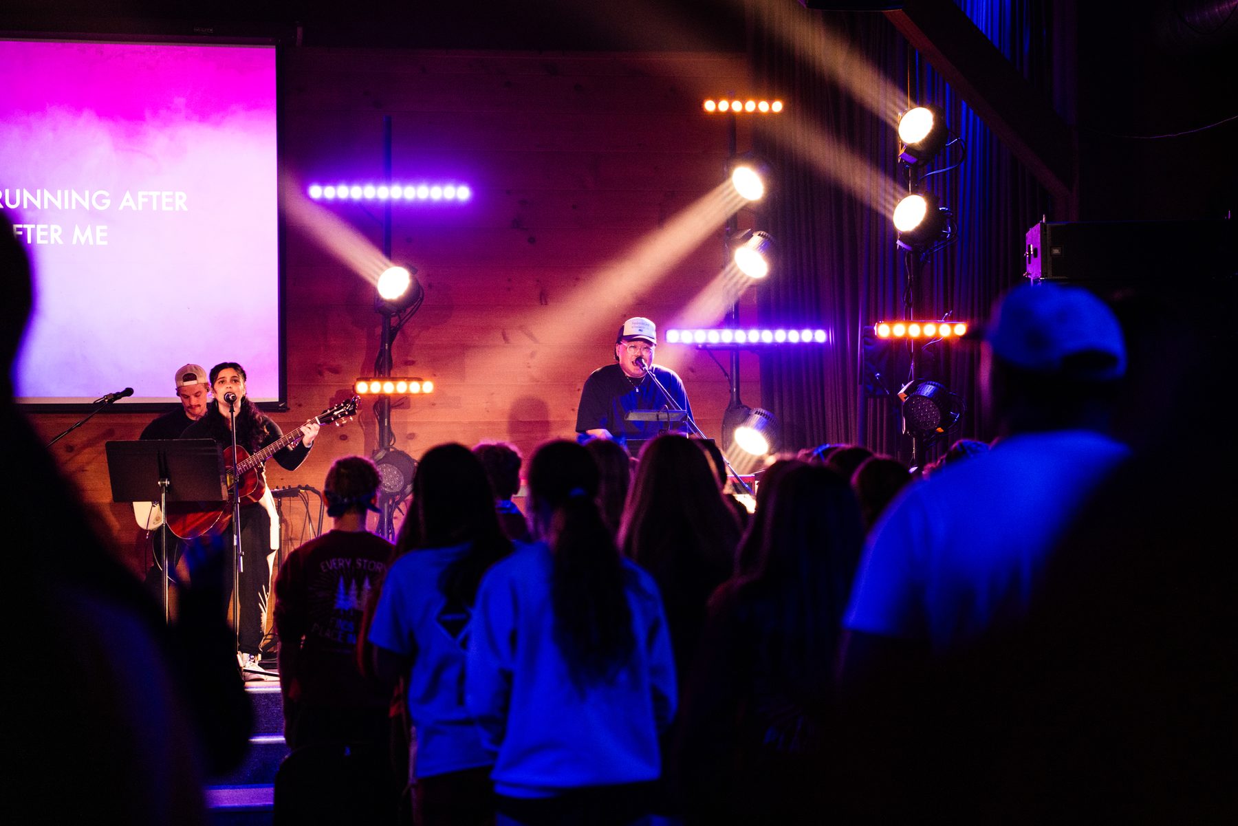 Worship set with purple and amber beams cutting through haze over the crowd