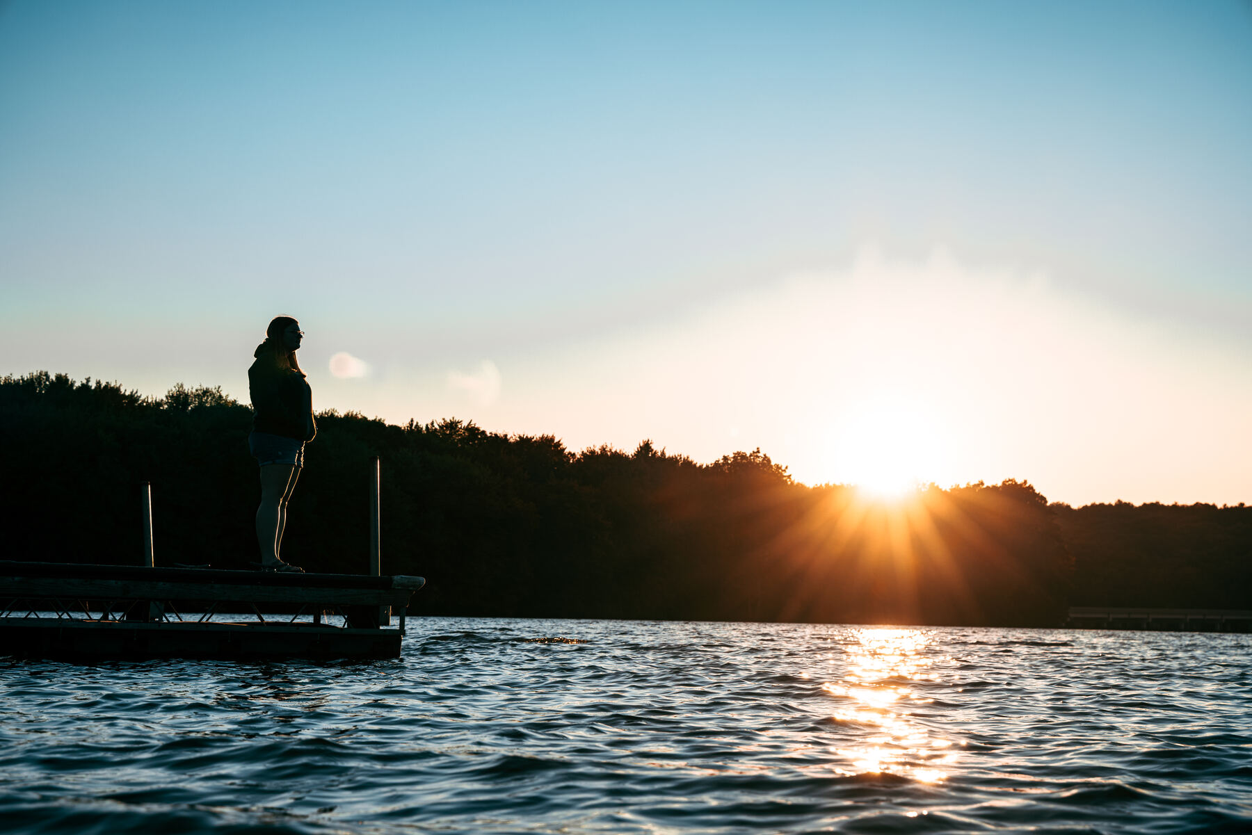 A figure silhouetted on a dock at sunset over a lake